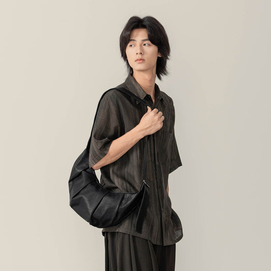 A person holding a black pleated waxed leather croissant bag with a shoulder strap.