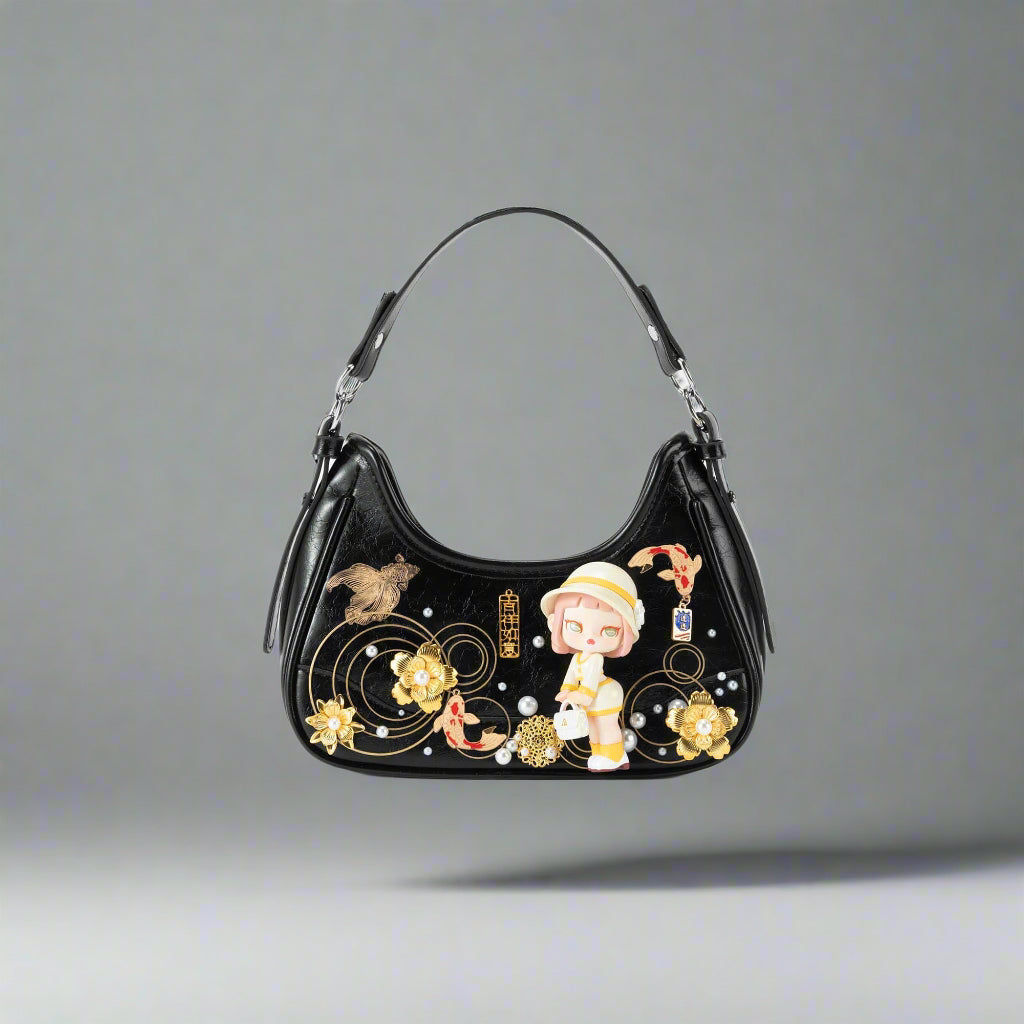 A black hobo bag with gold-tone koi fish, floral, and charm embellishments, featuring a three-dimensional doll figure on the front panel and silver-tone hardware.