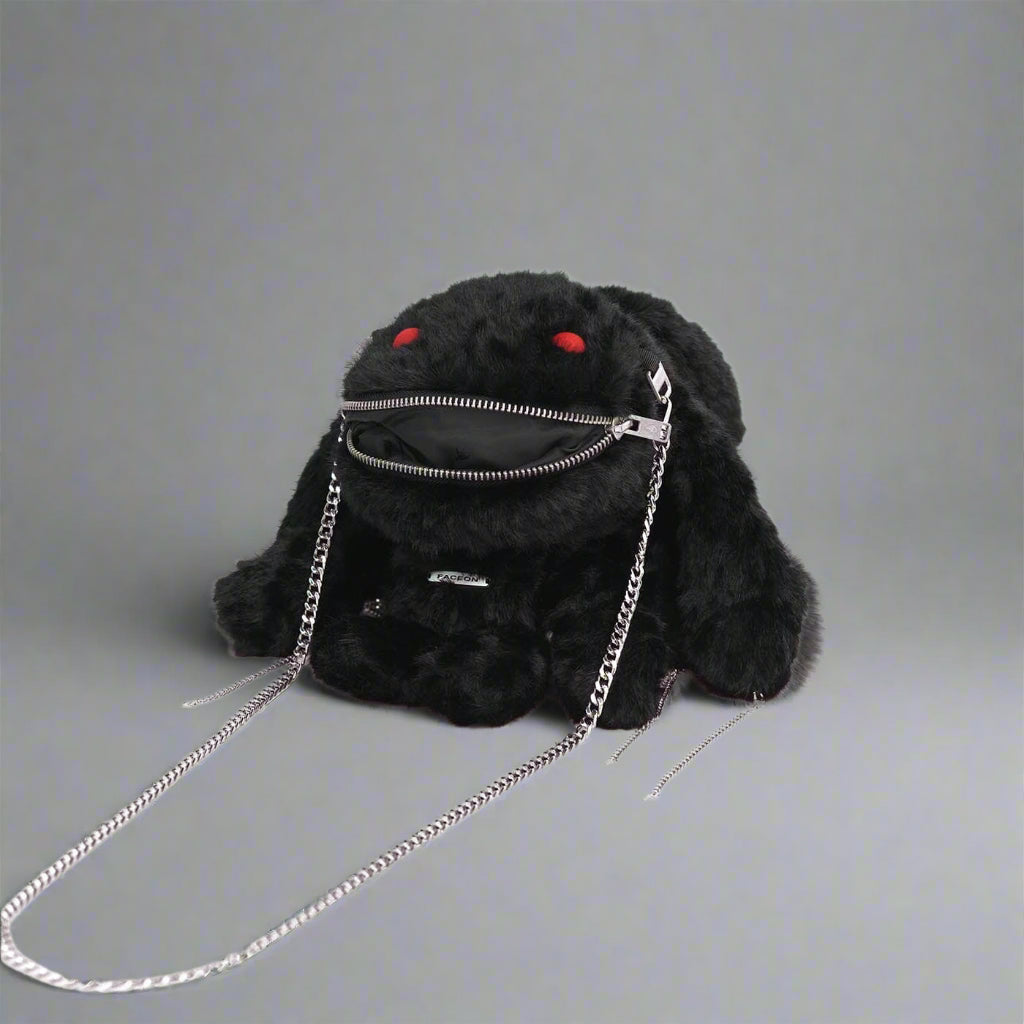 A black plush crossbody bag with a playful design featuring red eyes, zipper decoration on the mouth, and metal chains attached to the ears and sides.