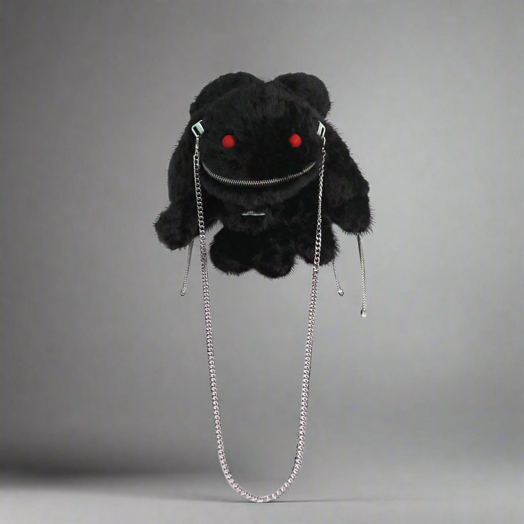 A black plush crossbody bag with a playful design featuring red eyes, zipper decoration on the mouth, and metal chains attached to the ears and sides.