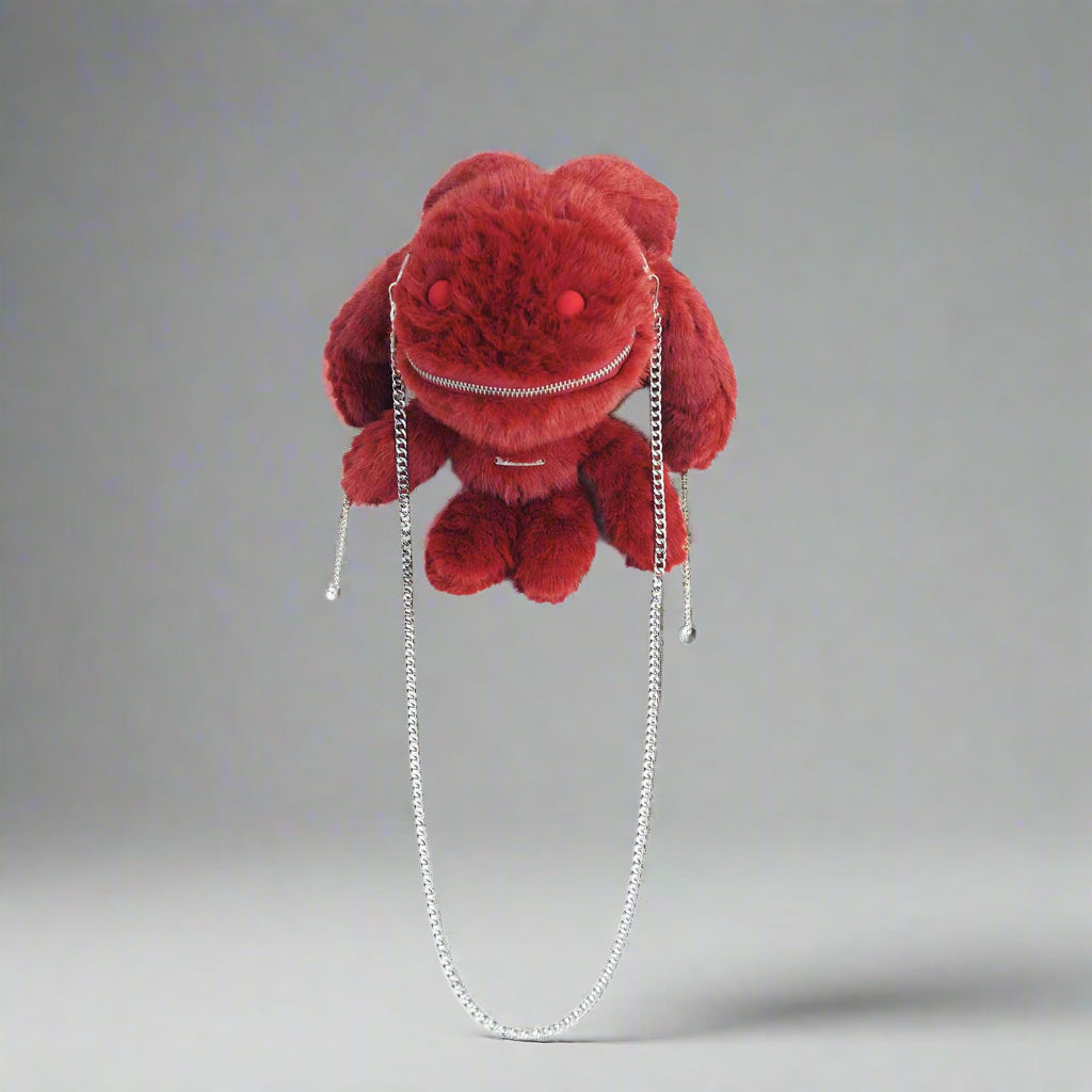 A red plush crossbody bag with a playful design featuring red eyes, zipper decoration on the mouth, and metal chains attached to the ears and sides.