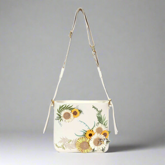 A white synthetic leather crossbody bag with a bohemian-inspired embroidered sunflower design on the front panel, featuring an adjustable shoulder strap and a top zip closure.