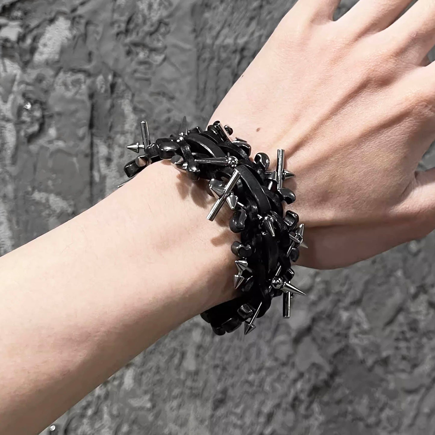 A black braided leather bracelet with metal spikes, worn on a wrist against a textured grey background.