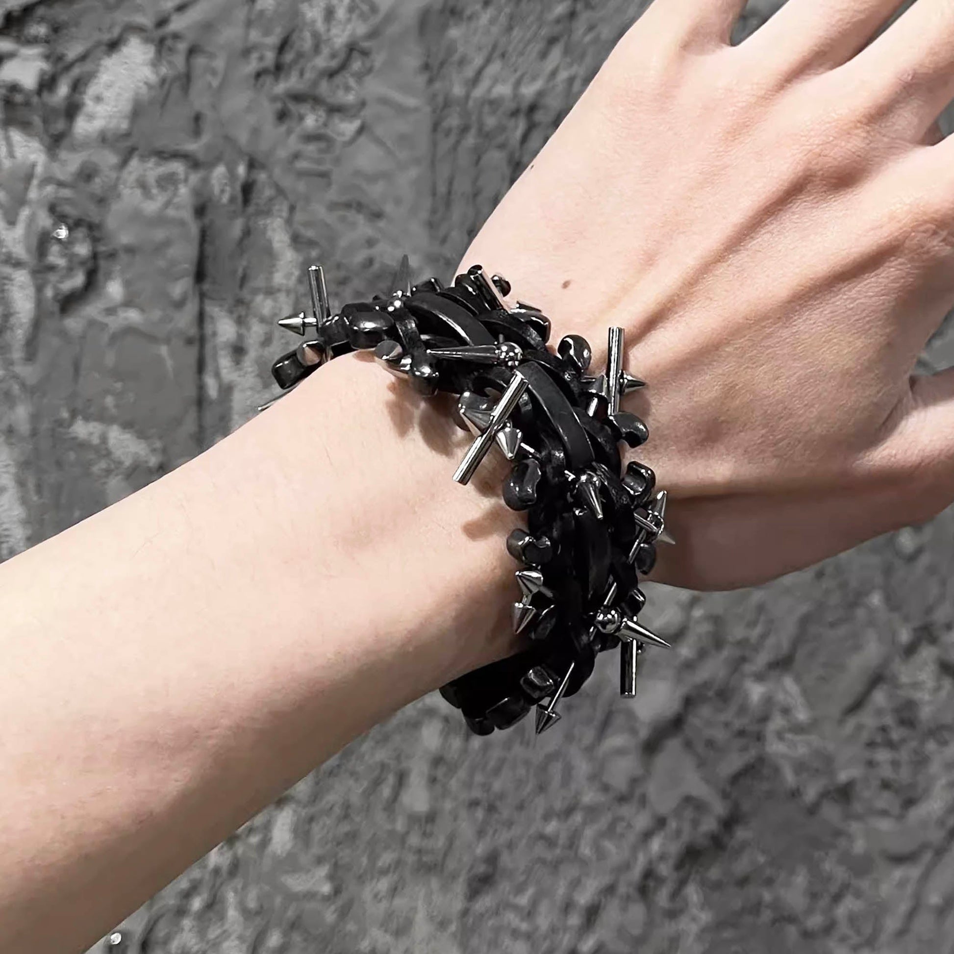 A black braided leather bracelet with metal spikes, worn on a wrist against a textured grey background.