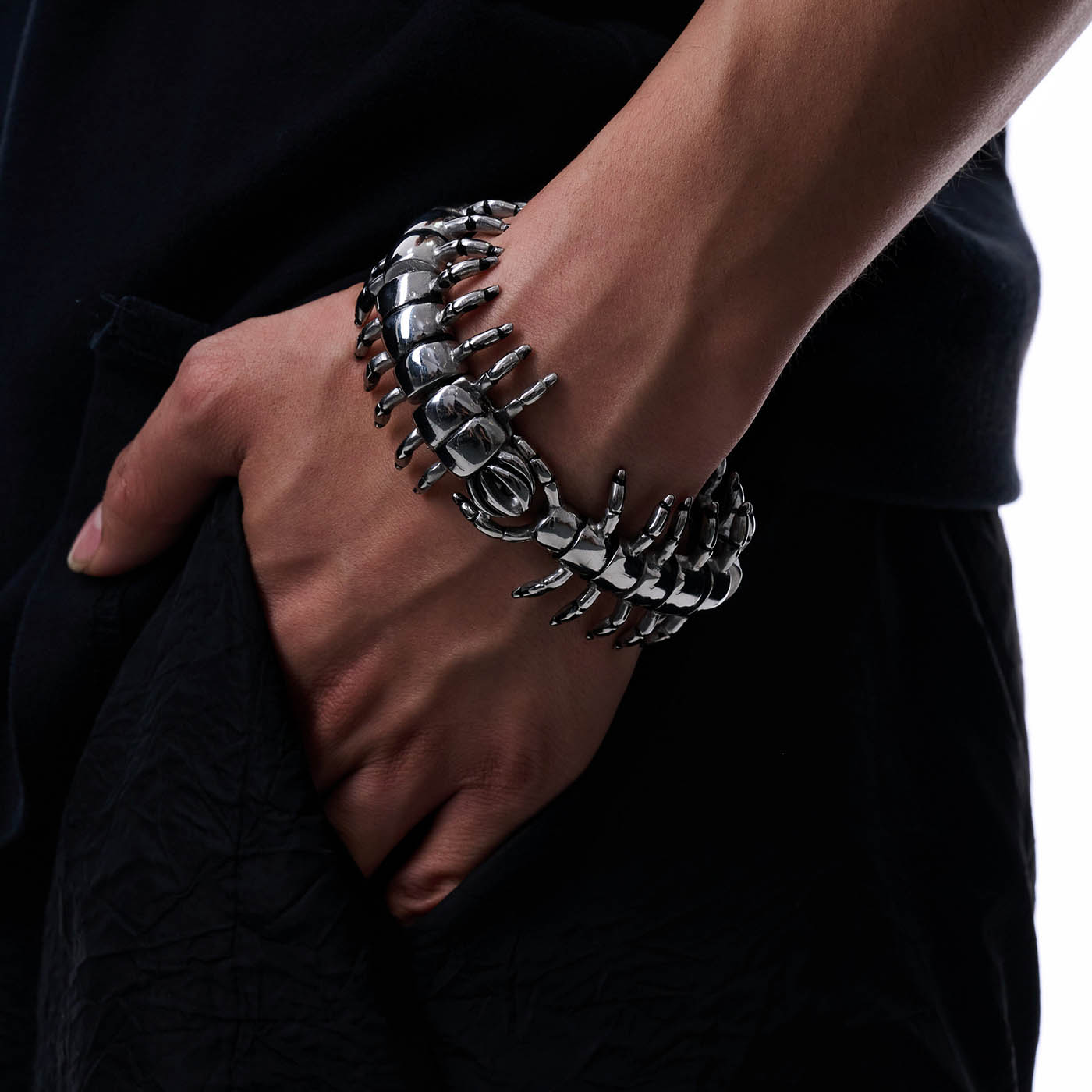 A person's wrist wearing a silver-colored metal bracelet with a geometric and intricate pattern, resembling a centipede or spine structure.