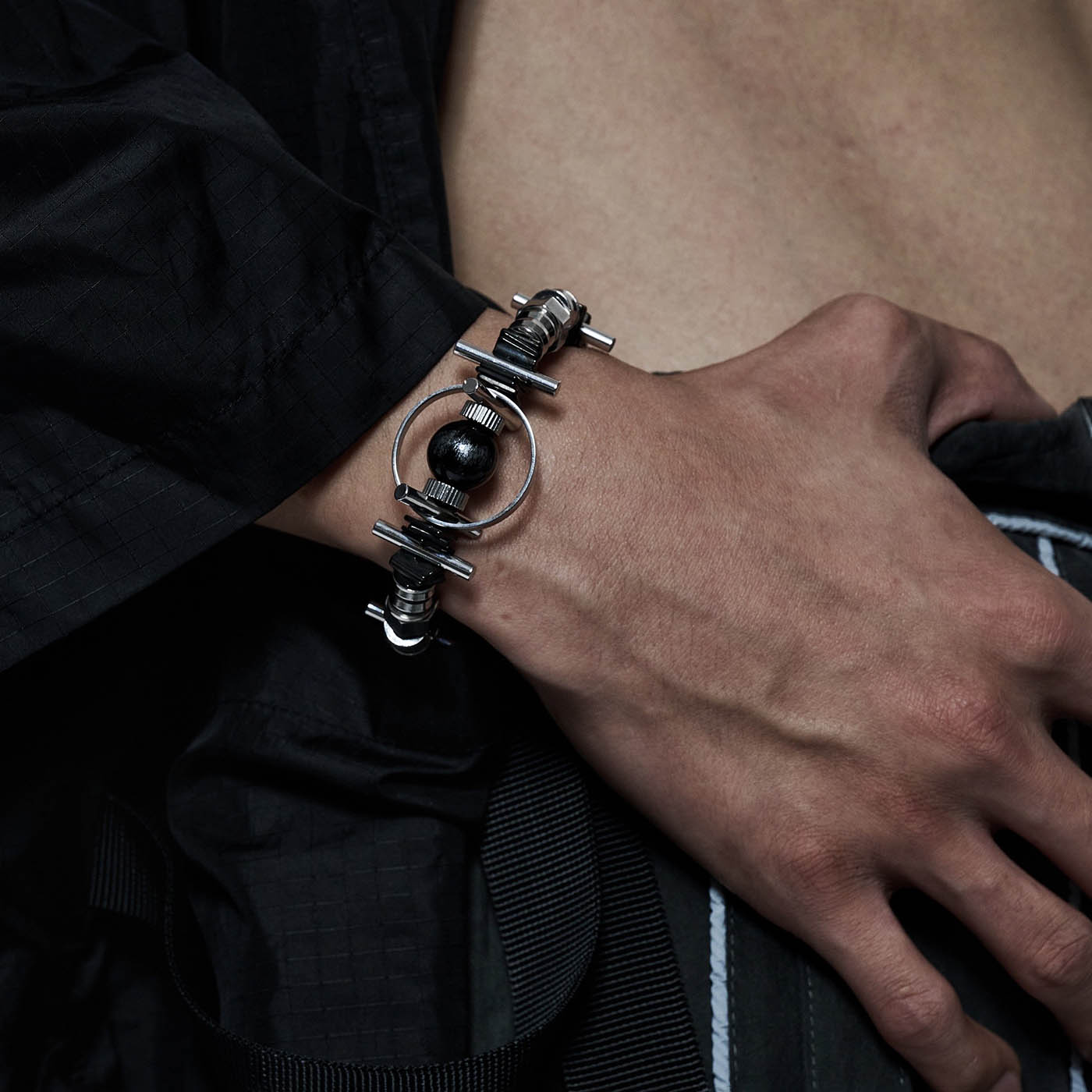 A close-up image of a person's wrist wearing a black and silver mechanical bracelet with a blackhole design.