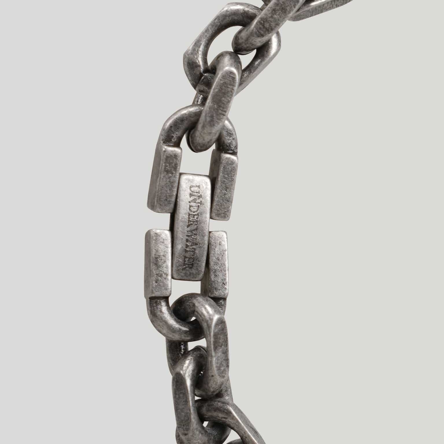Close-up of a vintage gunmetal chain bracelet with an engraved logo plaque.