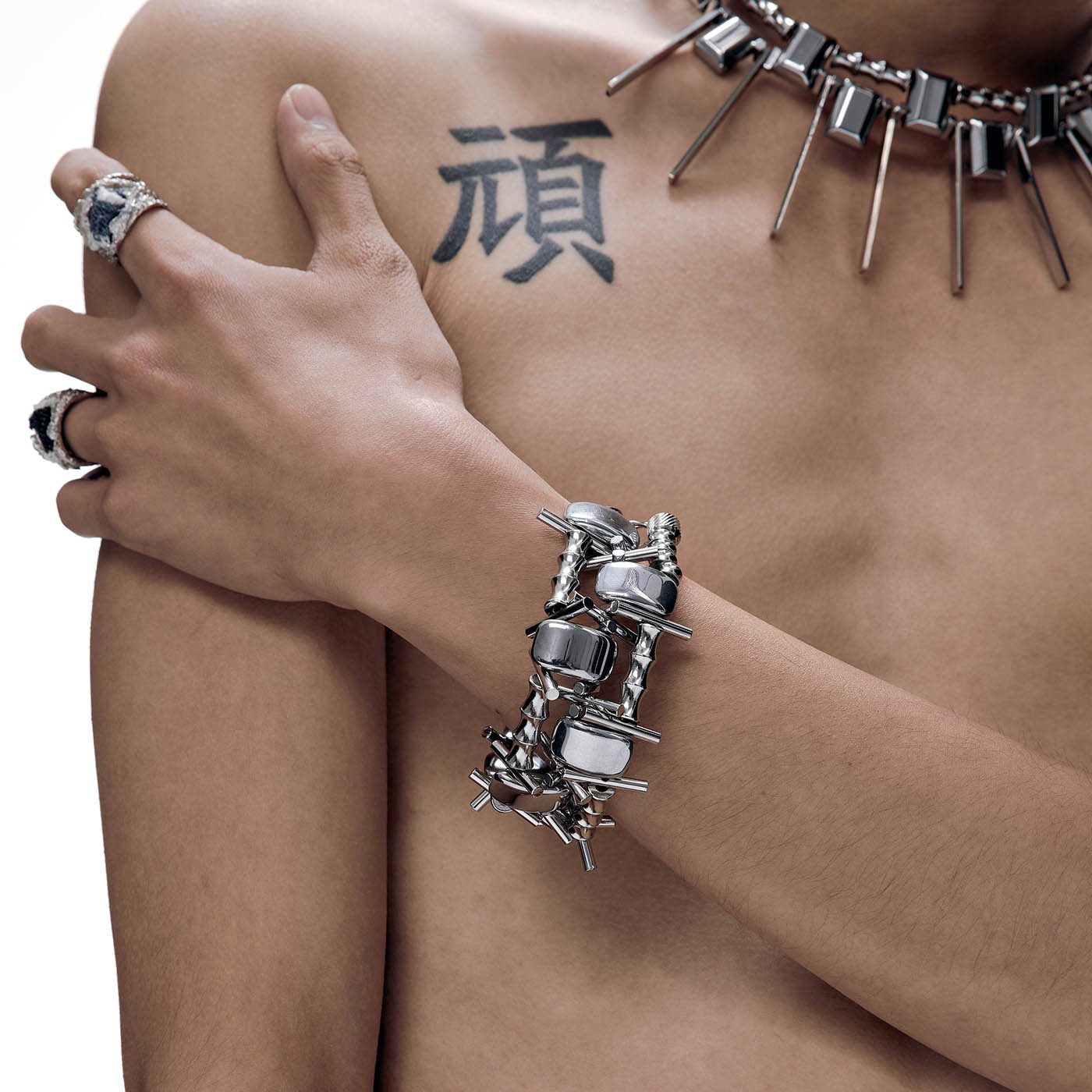 A close-up image of a person's forearm adorned with a silver mechanical bracelet featuring chains, gears, and sharp metal spikes.