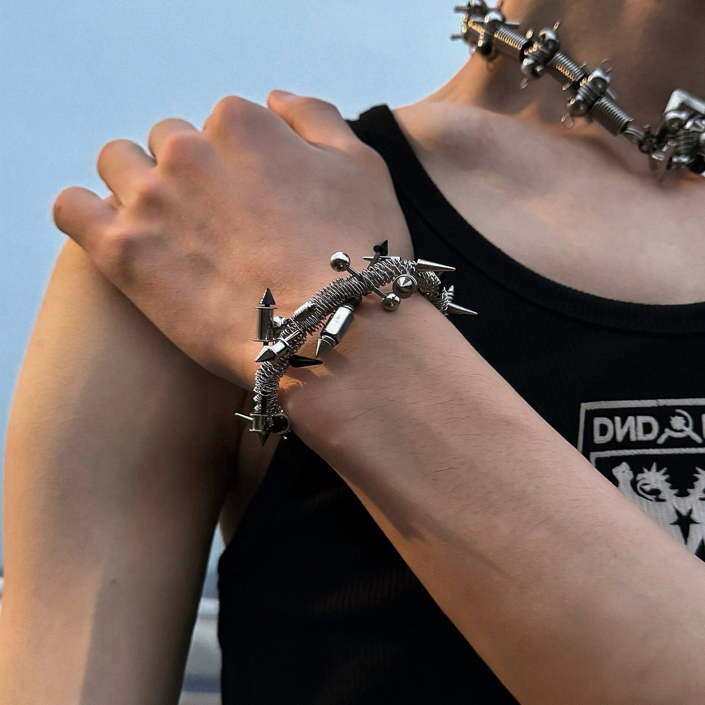 A person wearing a black top and showcasing a silver-colored hollow-out bracelet with rivet designs on their wrist.