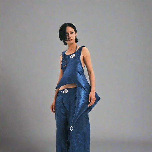 A person wearing a blue metallic thorn-like crossbody bag with a logo detail.