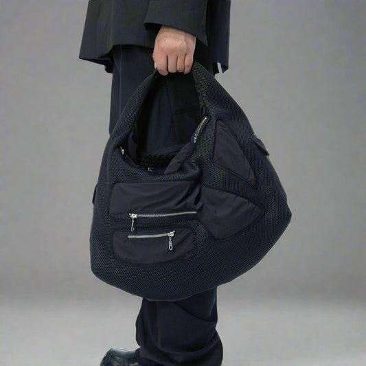 A person holding a large black multi-pocket utility bag with a modern design.