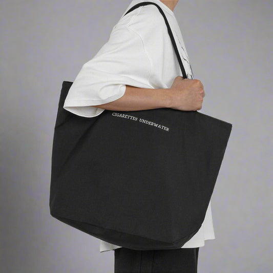 A person holding a large black tote bag with the text 'UNDERWATER' on it.