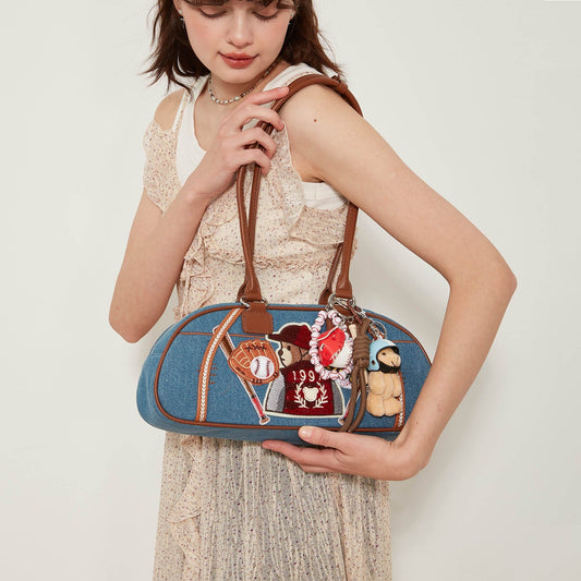 A person holding a blue denim bowling bag with faux leather detailing and a variety of pins attached to it.