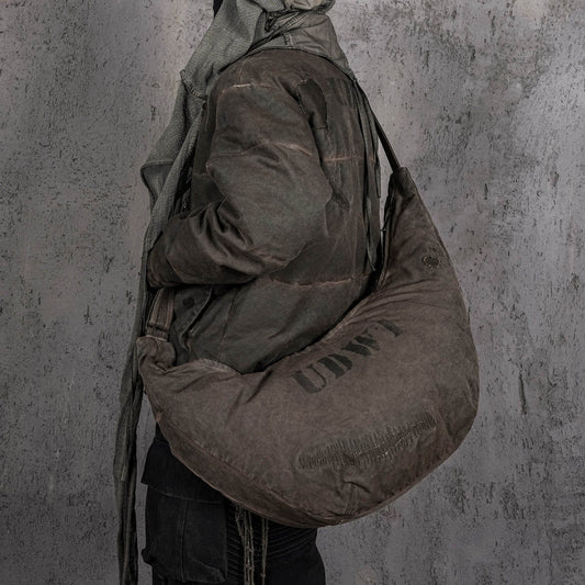 A person wearing a brown crescent-shaped distressed wanderer bag with patchwork details and an adjustable strap.