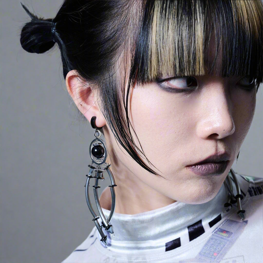 A person wearing a large, intricate silver earring with a black spherical bead.