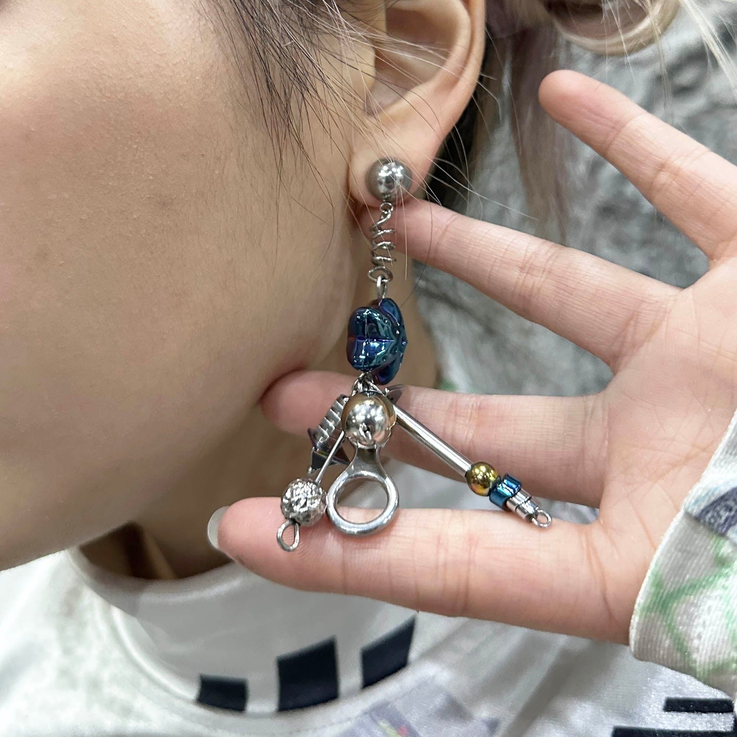 A person holding a semi-circular blue earring with a pendant and metallic charms