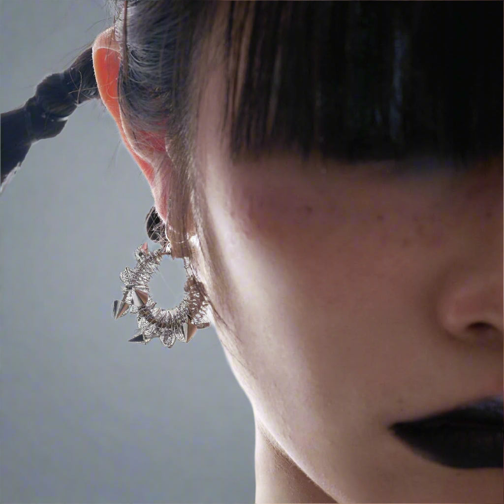 A side profile of a person wearing a hat and a large silver-colored earring with a geometric and spring-like design.