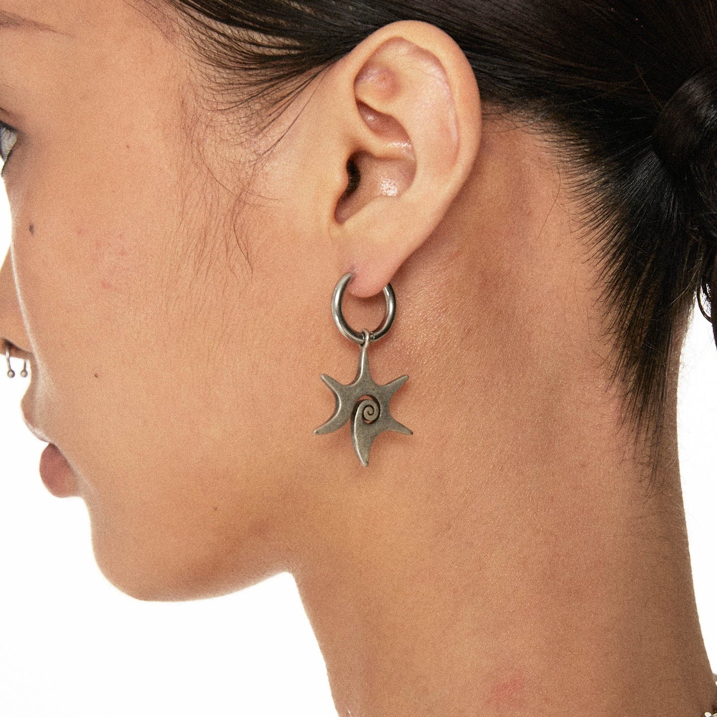 A close-up image of a woman's ear wearing a silver rustic hexagram swirl earring.
