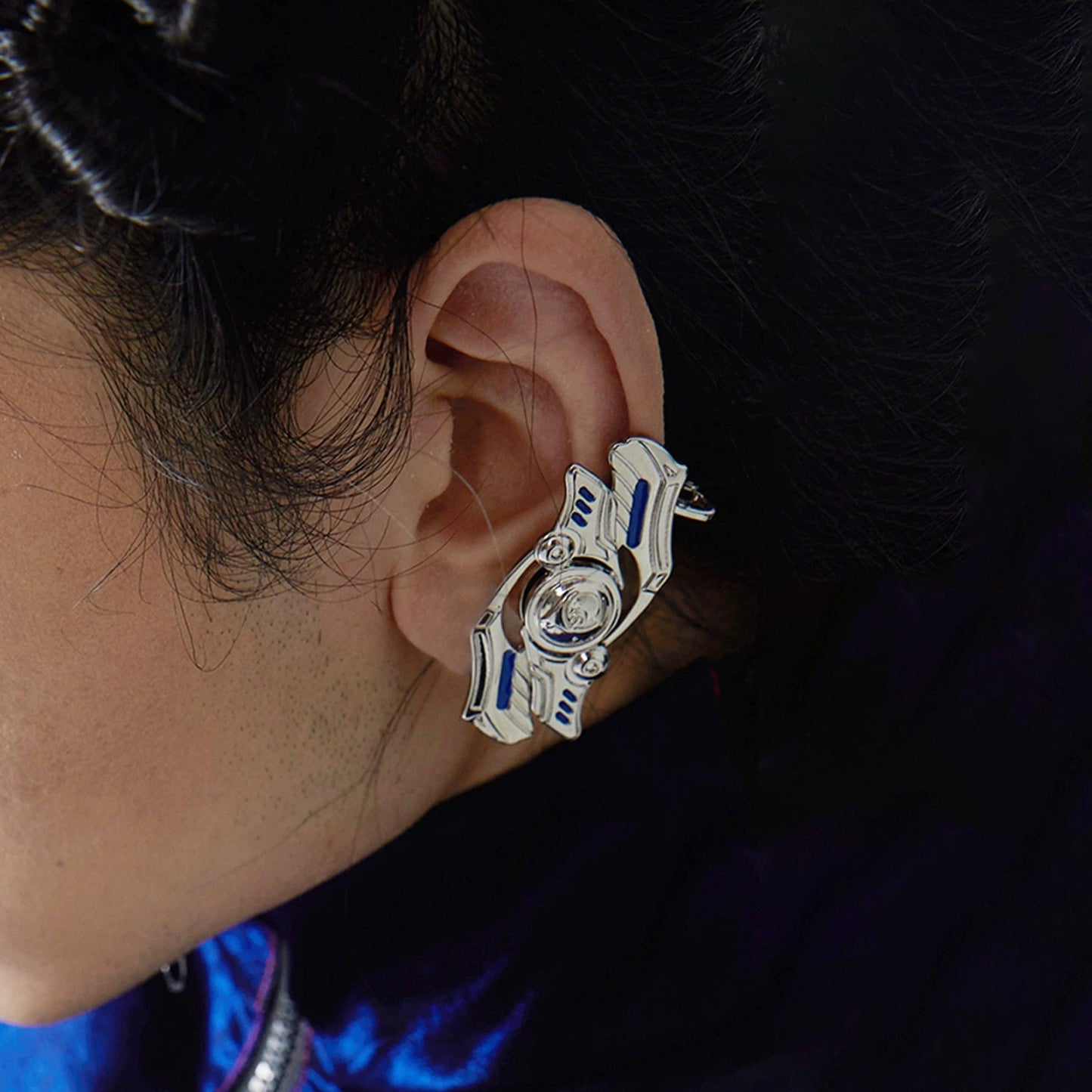 A person wearing a silver spinner earring with a geometric pattern.